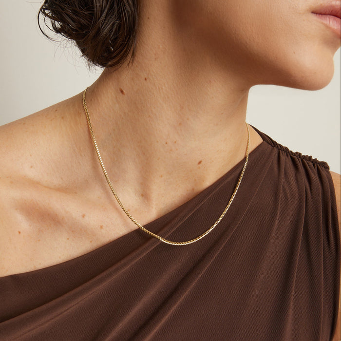 Model. Gold necklace worn by a person with a neutral background