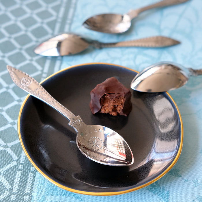 Bouchée au chocolat sur une soucoupe noire et or, avec des cuillères décorées tsé tsé
