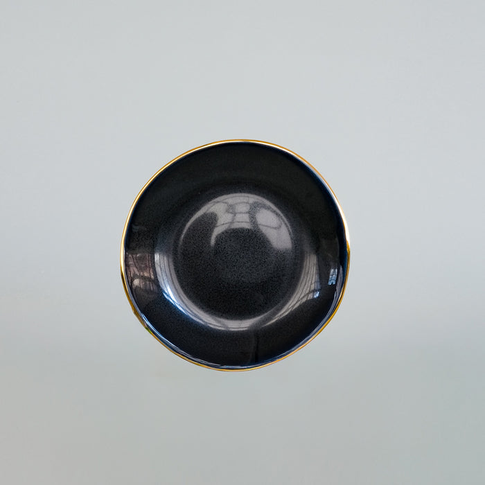 Soucoupe de forme irrégulière, noire avec bordure or. Tsé & Tsé