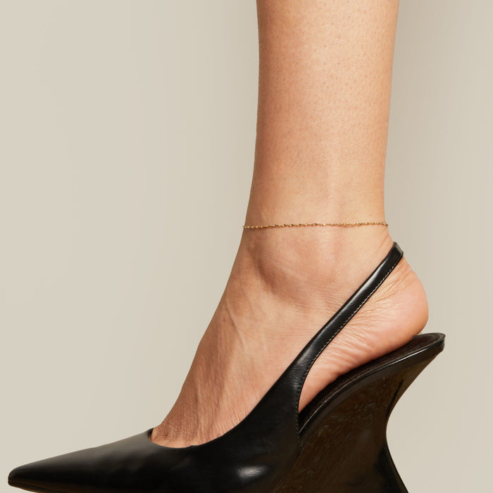 Model. Black wedge heel shoe and anklet worn by a person on a neutral background