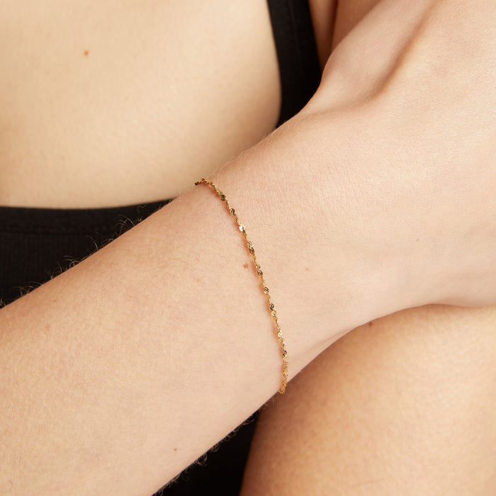 Model. Gold bracelet on a person's wrist against a neutral background.