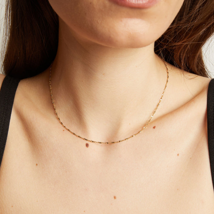 Model. Gold necklace on a person's neck with a neutral background.