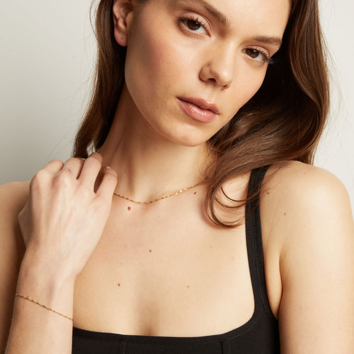 Model. Woman wearing a delicate gold necklace and bracelet against a neutral background.