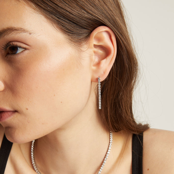 Model. Close up of a woman wearing tennis earrings with a neutral background.