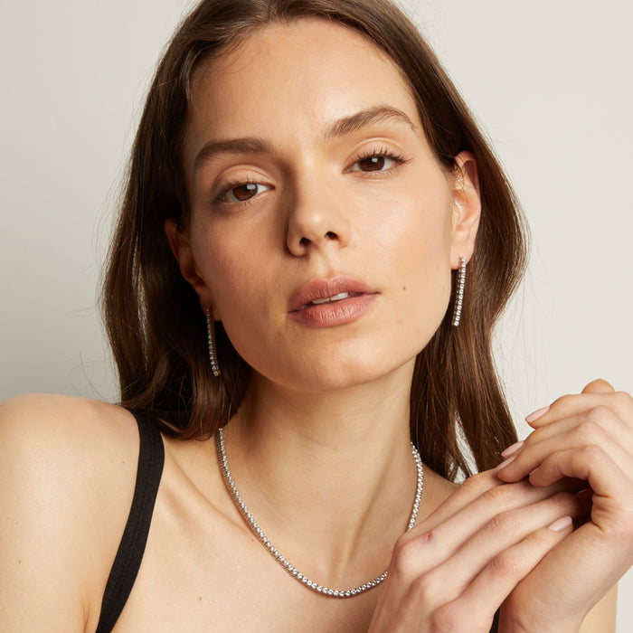Model. A woman wearing tennis earrings and necklace with a neutral background.