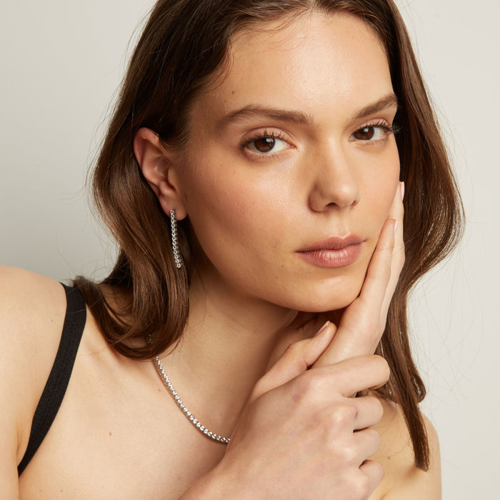 Model. A woman wearing tennis earrings and necklace with a neutral background.