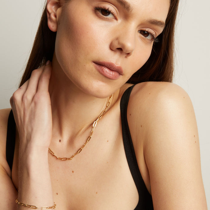 Model. Woman wearing a gold necklace with a plain background.