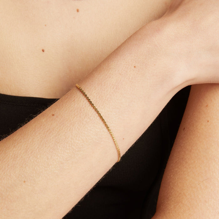 Model. Gold bracelet on a person's wrist with a neutral background.